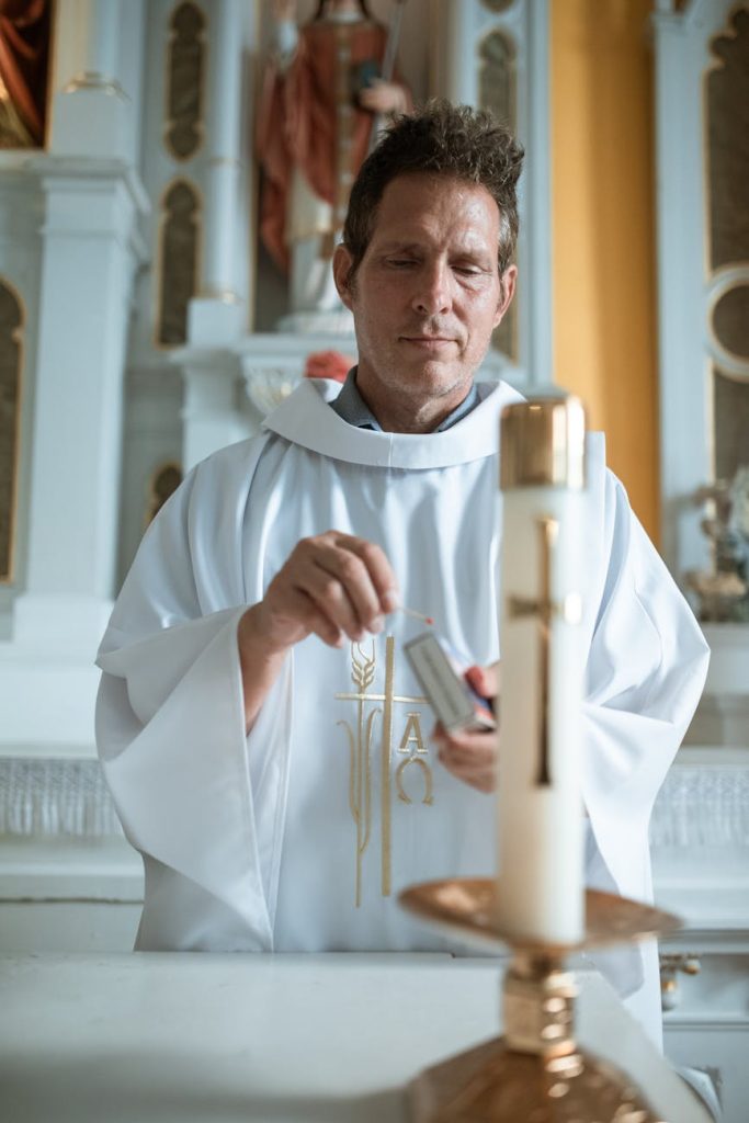 A devoted priest lights a candle during a solemn church ceremony, symbolizing faith and spirituality.